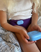 Load image into Gallery viewer, Child holding a blue Pjama speaker with a Pjama underwear with sensor attached.