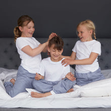 Load image into Gallery viewer, Three children in matching grey Pjama pants sitting on a bed.