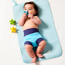Load image into Gallery viewer, Baby lying on a blue mat with toys around, wearing swim shorts.