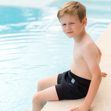 Load image into Gallery viewer, Young boy in black swim shorts sitting by a pool